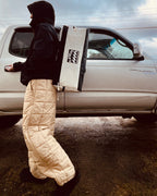 Person in winter clothing standing next to a vehicle with a large bag on their back. Made in Nova Scotia, Canada.